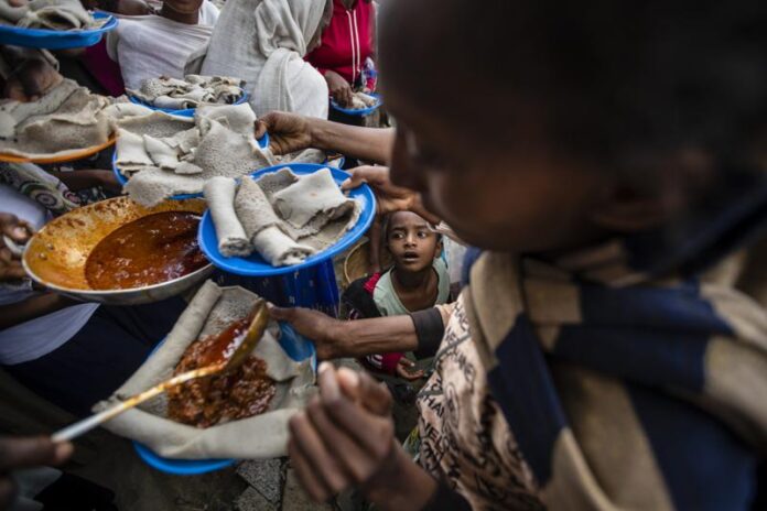 A young boy looks up as displaced Tigrayans line up to receive food donated by local residents at a reception center for the internally displaced in Mekele, in the Tigray region of northern Ethiopia, on Sunday, May 9, 2021. The 15 kilograms of wheat, half a kilogram of peas and some cooking oil per person, to last a month — was earmarked only for the most vulnerable. That included pregnant mothers and elderly people. (AP Photo/Ben Curtis)