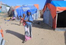 A woman carrying a child is seen at a camp on the outskirts of Mogadishu, capital of Somalia, on Jan. 13, 2022. (Xinhua/Hassan Bashi)
