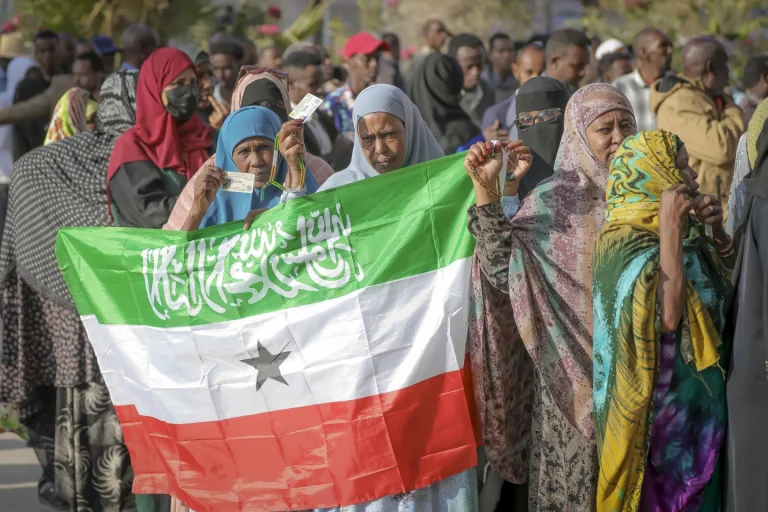 A woman displays the Somaliland flag as people queue to cast their votes during the 2024 Somaliland presidential election at a polling station in Hargeisa, Somaliland, Wednesday, Nov. 13,2024. (AP Photo/Abdirahman Aleeli)